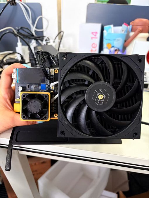 The image shows a person holding up a small computer fan, which appears to be a custom-built machine with a black color scheme. The fan has a unique design that sets it apart from typical fans found in computers. It is placed on a white desk next to some boxes and other items. The post about the silent, stable, and custom Black Knight Nerd QX seems to be related to this image as it features a comparison between the custom-built computer fan and the post's description of the machine.