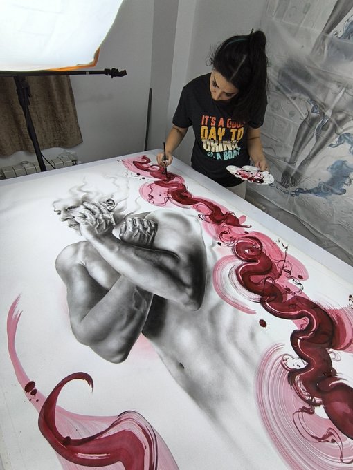 A female artist wearing a "IT'S A GOOD DAY TO BE SOMEONE'S MOMMY" t-shirt paints a large canvas depicting a grayscale classical sculpture intertwined with flowing red ribbon-like forms.