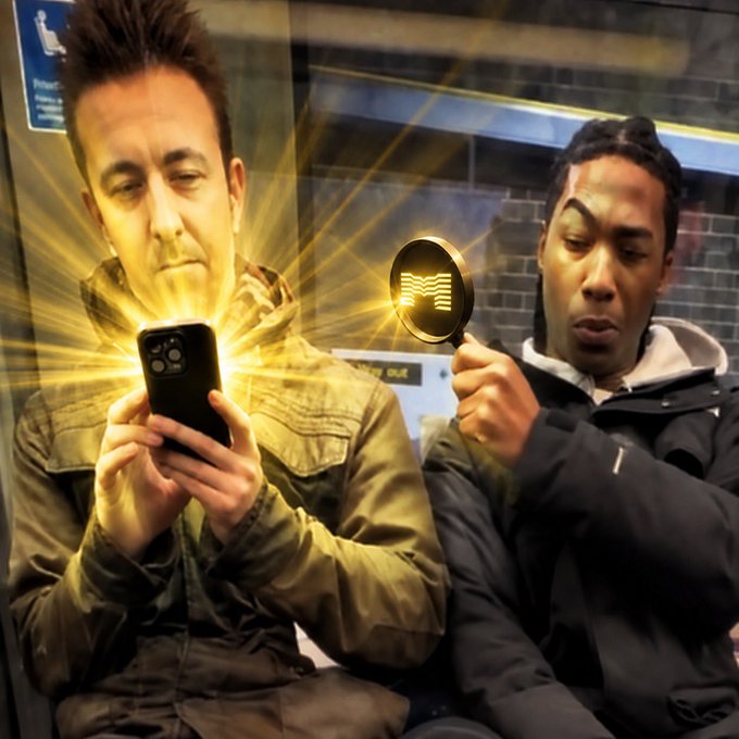 Two men sit on a subway train; one looks at his phone while a digital burst effect emanates from the screen, and the other holds a round black mirror or sign featuring a wave logo.
