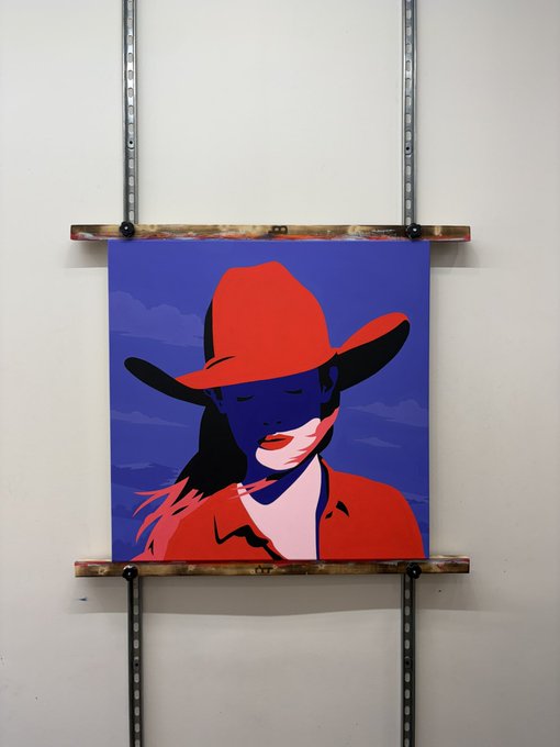 A pop-art style painting of a woman in a red cowboy hat against a purple sky, mounted on a wall using a metal rail and wooden support system.