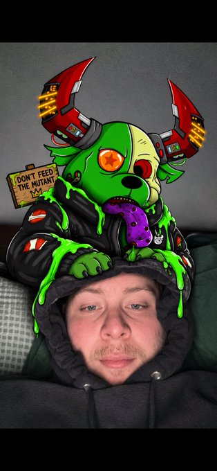 A man in a dark hoodie is in the background while a large, cartoonish green zombie dog head with red mechanical ears and a purple tongue is digitally overlaid on top of his head, alongside a small sign reading 'DON'T FEED THE MUTANT!'.