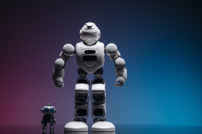 3D render of a humanoid robot with white armor and exposed mechanical joints standing next to a smaller black robot against a purple-blue gradient background.