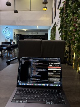 A laptop displaying lines of code sits on a wooden table in a modern, plant-filled lounge, with the developer likely reflecting on the growth that comes from building something from scratch. The serene workspace echoes the post's sentiment of gratitude for a life once only dreamed of—now realized through focused, quiet productivity.