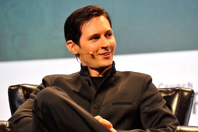Pavel Durov, founder of Telegram, sits on a stage with a headset microphone, appearing relaxed and smiling during a panel discussion. The image ties to the news of Telegram expanding its cryptocurrency services to over 1 billion users through a native "Gram" non-custodial wallet.