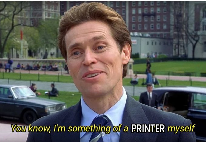 A man in a gray suit and blue tie speaks directly to the camera with a confident expression, set against an outdoor campus background with cars and pedestrians. The caption reads, "You know, I'm something of a PRINTER myself," a famous *Spider-Man* quote cleverly modified to riff on the post's joke about not having enough printers.