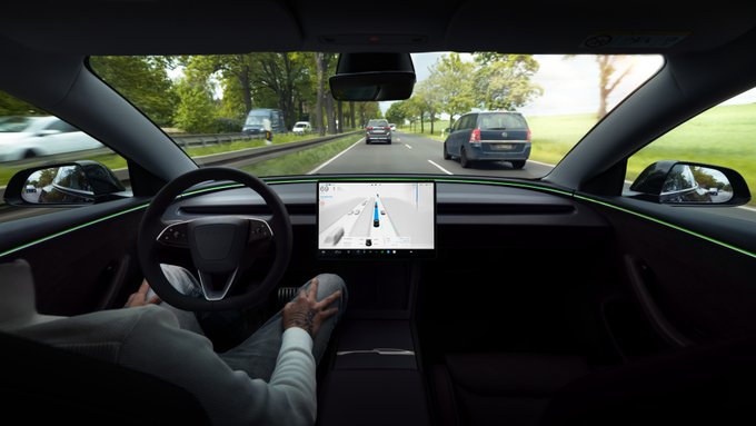 Interior view of a Tesla vehicle with a driver holding the steering wheel, showing the central touchscreen displaying the road and surrounding traffic on a multi-lane highway.
