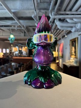 A shiny purple and green Bored Ape figurine wearing pink ski goggles sits on a table at an event venue. The colorful mascot reflects the fun social gathering shared by the Bored Ape community at the Shanghai meetup mentioned in the post.
