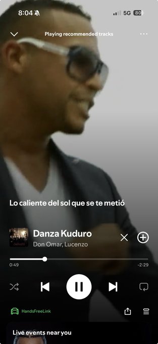 A Spotify mobile interface showing the song 'Danza Kuduro' by Don Omar and Lucenzo playing, with Spanish lyrics displayed on screen and a LIVE indicator at the bottom.