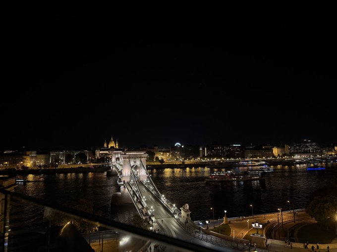 A nighttime view of the Chain Bridge in Budapest with city lights and the Danube river below.