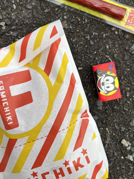 Discarded litter on asphalt includes a crumpled 'FOMICHIKI' paper wrapper with red and yellow graphics, a small red and yellow 'Bigfoot' wrapper, and an empty plastic-wrapped snack stick.