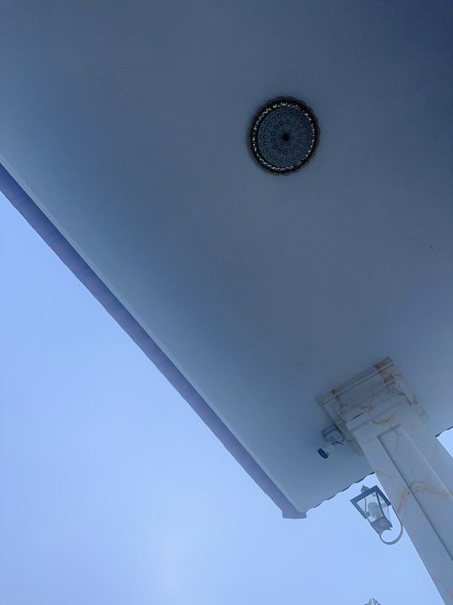 A low-angle shot captures a round, ornate ceiling light fixture against a white ceiling and pale blue sky.