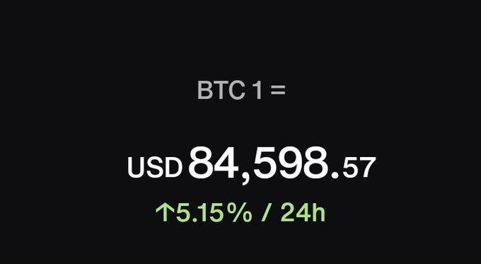 A dark screen displays the Bitcoin price as 'BTC 1 = USD 84,598.57' with a 24-hour increase of 5.15% shown in green.