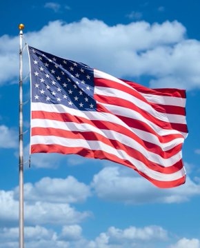 The American flag waves in the wind against a bright blue sky filled with scattered white clouds.