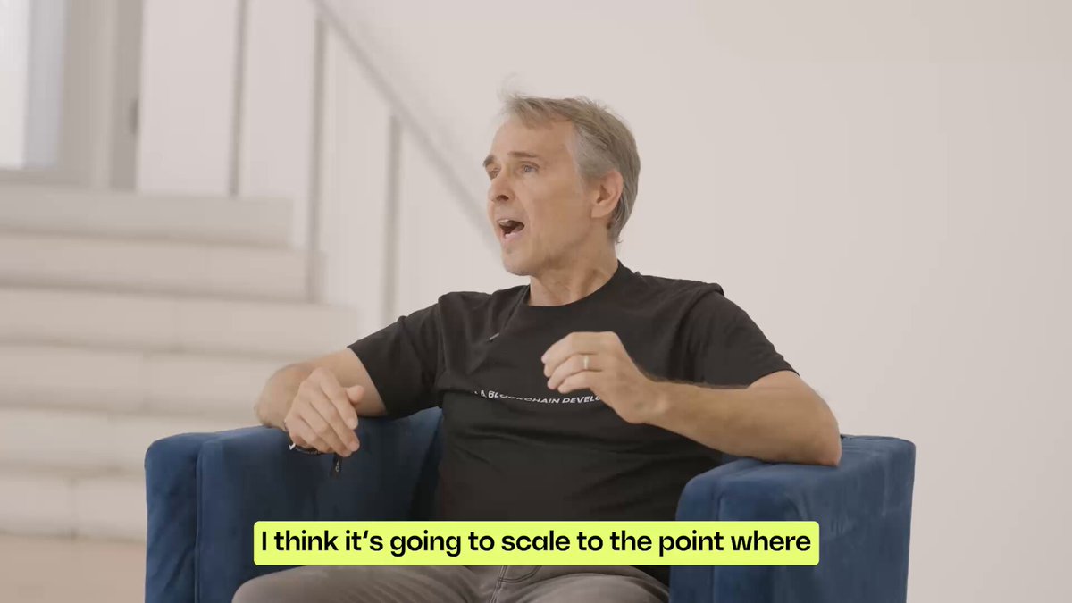 The image shows a man sitting in a blue chair with his arms crossed while talking on the phone. The caption below the image reads "I think it's going to scale to the point where".