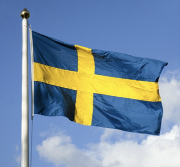 The national flag of Sweden, featuring a yellow Nordic cross on a blue field, waving against a blue sky.