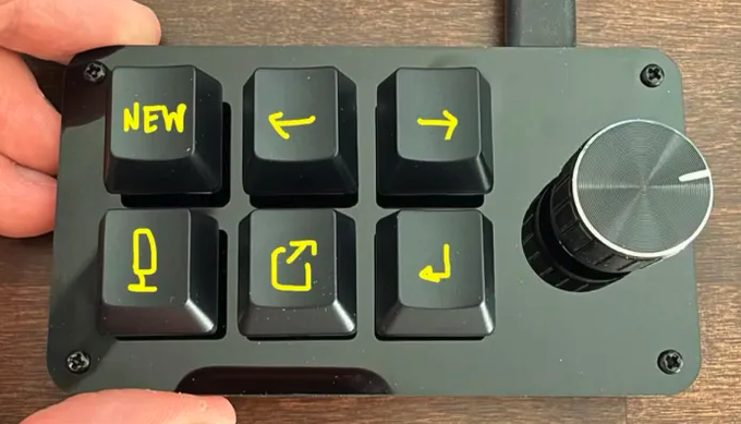 A DIY alternative to the $250 Codex Micro, this homemade macropad features six mechanical keys labeled "NEW," arrow symbols, a microphone icon, a share/export icon, and an enter key, alongside a sleek metallic rotary knob—mirroring the functionality of the original Codex device at a fraction of the cost.