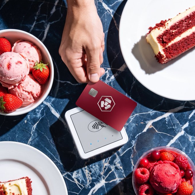 A hand taps a Crypto.com card on a payment terminal surrounded by desserts like strawberry ice cream, red velvet cake, and berry sorbet, illustrating how the card earns up to 5% back on everyday spending like dining and treats.