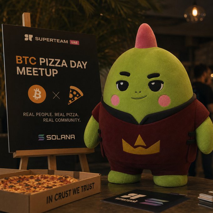 A green mascot with a red mohawk stands next to a 'BTC PIZZA DAY MEETUP' sign for Superteam UAE and Solana, with a pizza box labeled 'IN CRUST WE TRUST'.