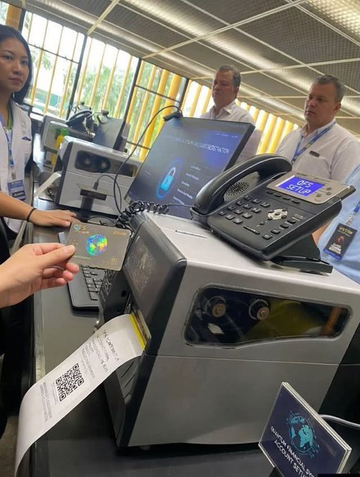 A person holds a credit card near what appears to be a customs or financial verification machine printing a label, with a sign reading 'QUARANTINE MEDICAL CHECK POINT (TBT)' visible.