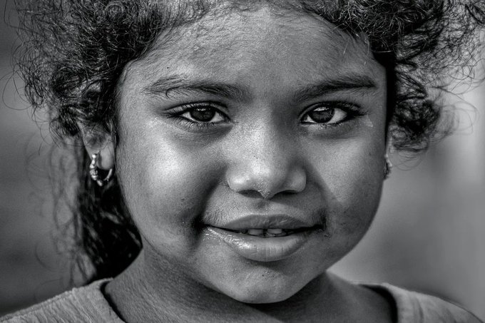 A black and white close-up portrait of a young woman with curly hair smiling gently at the camera.