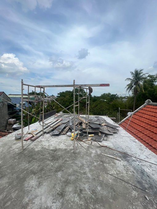 A rooftop construction site with metal scaffolding, scattered roof tiles, and tools under a cloudy sky.