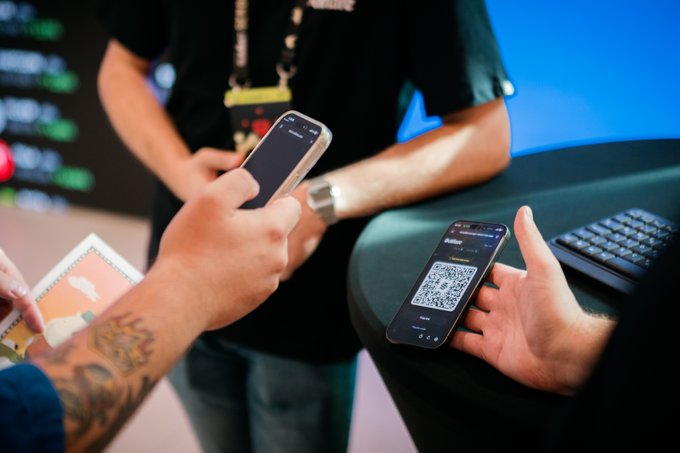 Two people scan a QR code on a smartphone displayed at the Solflare booth during the Solana Summit, with another phone showing the scanning process and a Solflare-branded keyboard nearby. The scene captures the in-person activation for the "Trade Your Way to $25K" promotion, where attendees can scan to claim 10 USDC and compete for $25,000 in trading rewards.