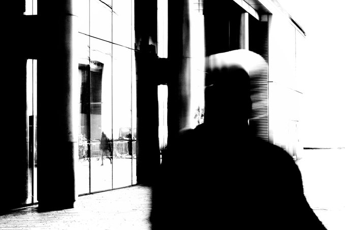 A high-contrast black and white image showing the blurred silhouette of a person in motion against bright window panels.