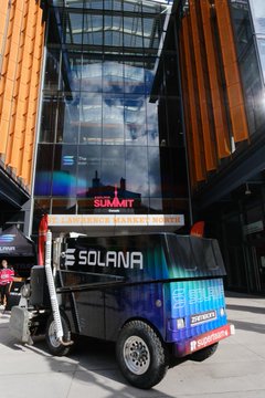 A small trailer with 'SOLANA' branding parked outside a modern building at a 'SUMMIT' event, promoting the cryptocurrency ecosystem.