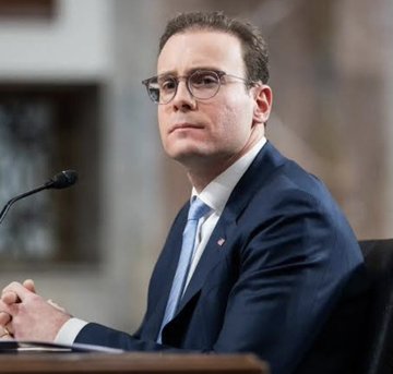 A man in a dark suit, white shirt, and light blue tie wearing glasses sits at a desk with a microphone, appearing to testify or speak at a formal hearing. While the post mentions the CFTC's announcement regarding XRP software developers, no specific text, names, or identifying details are visible in the image to directly connect it to that announcement.