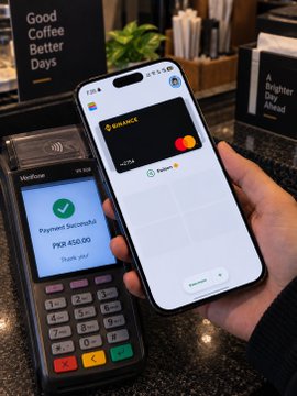 A hand holds an iPhone displaying a digital wallet/Apple Pay card over a Verifone payment terminal that shows 'Payment Successful' for PKR 450.00, with a 'Good Coffee Better Days' sign in the background.