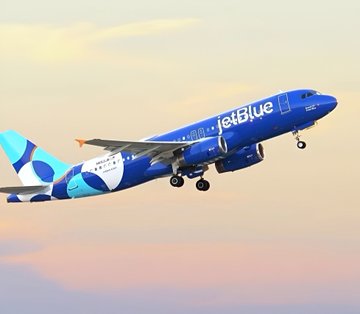 A JetBlue airplane, featuring its blue livery with "JetBlue" text on the fuselage, ascends against a sunset sky—illustrating the post's news that Strive ($ASST) has surpassed JetBlue's market cap with a record $1.91 billion valuation.