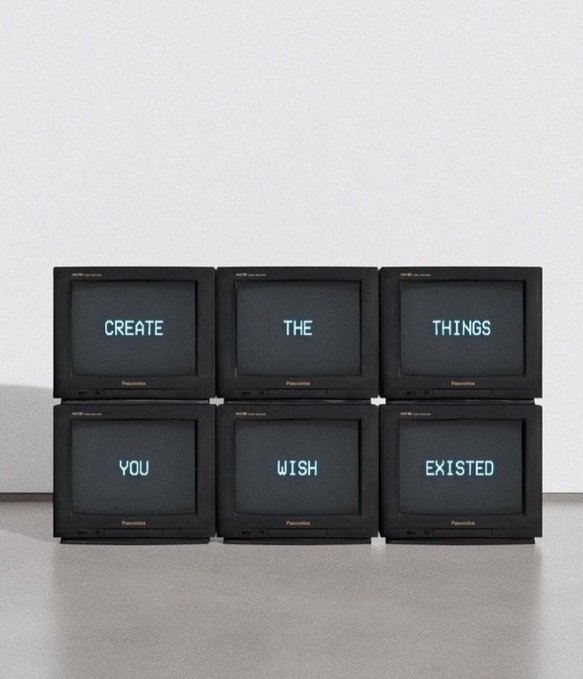 Six vintage CRT monitors stacked in two rows display the phrase "CREATE THE THINGS YOU WISH EXISTED" in glowing cyan text across their screens.