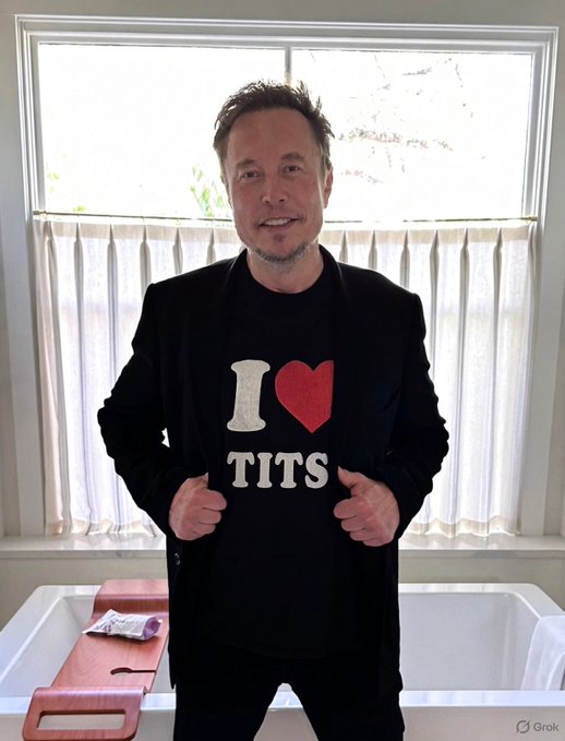 Elon Musk stands indoors wearing a black blazer over a black t-shirt that reads 'I ❤️ TITS'. The image has a 'Grok' watermark in the corner.