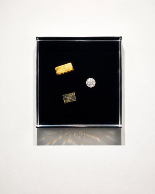 The image shows three small metallic items—a gold bar, a silver coin, and a microchip—displayed within a black, illuminated square frame mounted on a white wall. The piece visually echoes the "More Markets. One Place." tagline by juxtaposing traditional commodities (gold and silver) with modern technology (the chip), symbolizing a unified marketplace that bridges classic and digital assets.