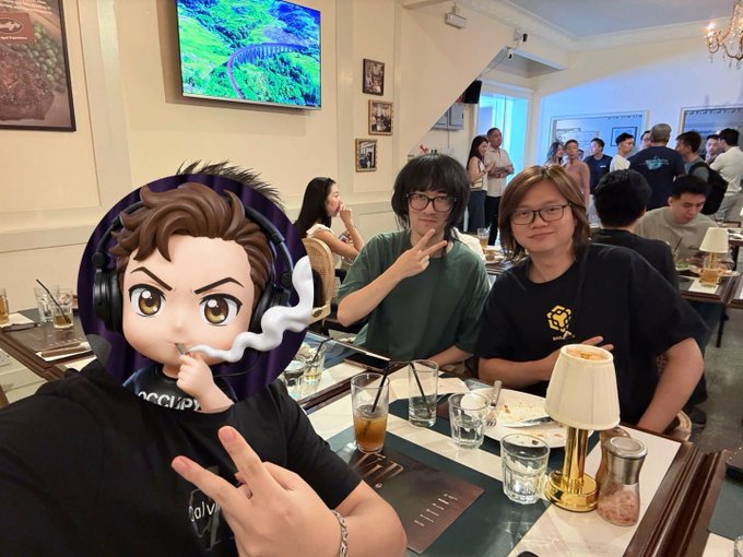 A casual photo taken at a restaurant showing two young men posing with peace signs, with one person's face obscured by a cartoon avatar of a person wearing headphones smoking.