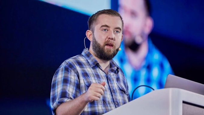 A bearded man wearing a blue plaid shirt speaks at a podium with a headset microphone, appearing to give a presentation. The image likely shows a Chainlink or LayerZero executive addressing the audience, contextualizing the post about the $292 million Kelp DAO bridge exploit involving Lazarus Group and cross-chain bridge vulnerabilities.