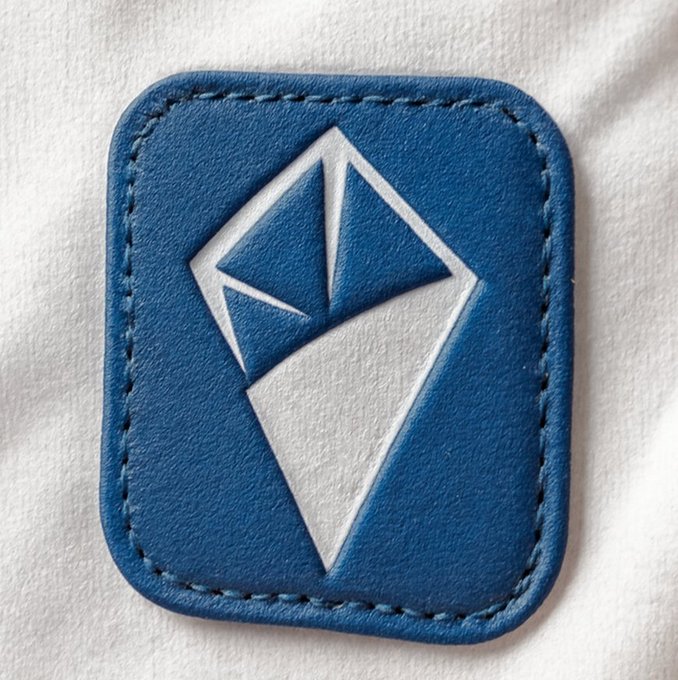 A blue leather patch with a stylized white geometric crystal/diamond logo, stitched onto a white fabric background.