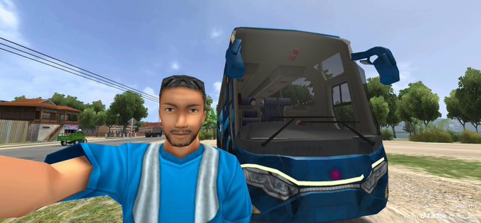 A 3D video game screenshot showing a man in a blue shirt taking a selfie in front of a blue bus in a rural town setting.