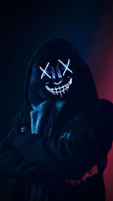 A dark, hooded figure wearing a glowing LED mask with X-shaped eyes and a stitched smile, lit by blue and red neon lights.