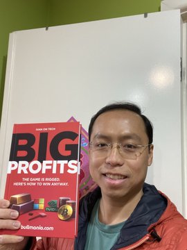 A smiling man with glasses holds up a red book titled 'BIG PROFITS!' with the subtitle 'THE GAME IS RIGGED. HERE'S HOW TO WIN ANYWAY.' and 'boomerang' text on the cover.