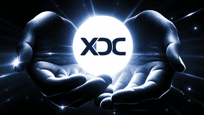 Two cupped hands cradle a glowing orb displaying the "XDC" ticker against a radiant blue background, symbolizing the XDC Network's partnership with Stripe subsidiary Bridge to integrate stablecoin payments, fiat exchange, and multi-currency custody for developers.