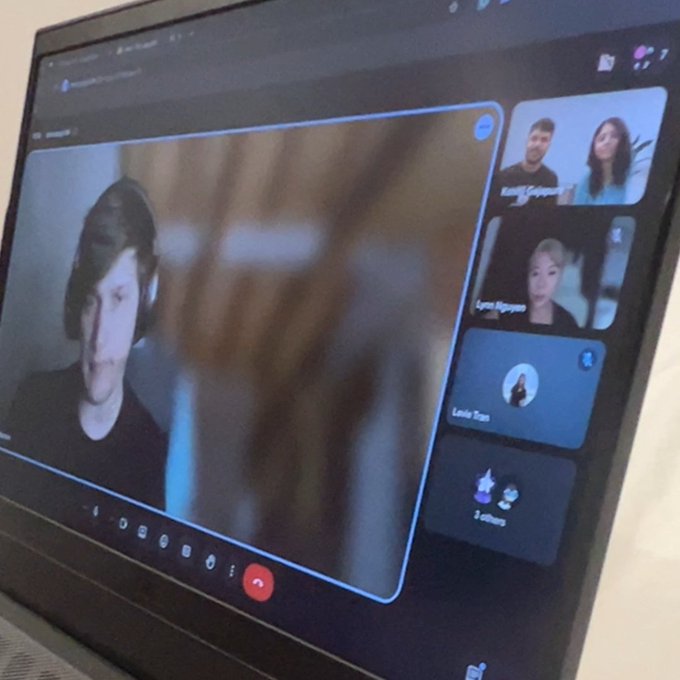 A laptop screen displays a video conference call with multiple participants.