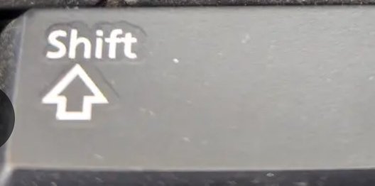 A close-up of a keyboard's Shift key on a dark laptop, showing the white upward arrow symbol and "Shift" label.