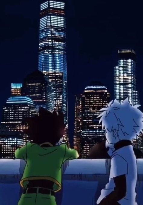 An anime scene shows two characters from behind, looking out at a brightly lit city skyline at night, with one character having white spiky hair.