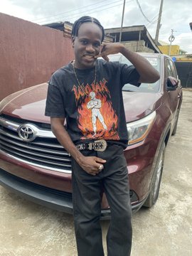 A young man wearing a black t-shirt featuring a fiery orange graphic design poses in front of a maroon Toyota SUV, showcasing his new $Wojak merch. The image complements his post celebrating his new $Wojak t-shirts from @W_o_j_a_k_CN and @wojakcto.