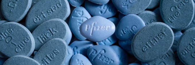 A close-up macro photograph of blue Pfizer-branded pills with the Pfizer logo embossed on them, some labeled as "100 mg."