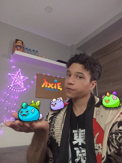 A young man poses in a room with purple lighting and an 'AXIS INFINITY' sign, with three cartoon character graphics floating around him.