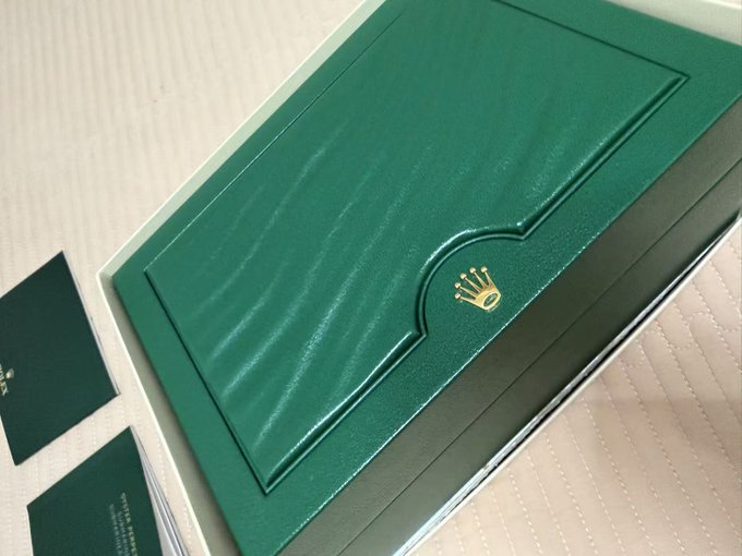A green Rolex box with the signature gold crown logo, shown alongside what appears to be accompanying documentation or warranty cards. The image relates to the post as the user humorously references receiving this luxury item by emphasizing that "GMGN is awesome," suggesting their positive experience with the GMGN platform made this possible.