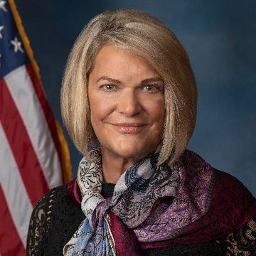 A formal portrait of Senator Cynthia Lummis standing in front of an American flag, accompanying her statement about "The Clarity Act" ensuring customers retain ownership of their crypto assets even if companies fail.