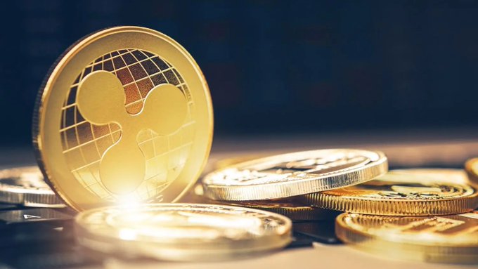 A close-up of gold coins, with a prominent Ripple (XRP) coin standing upright among scattered coins on a surface.
